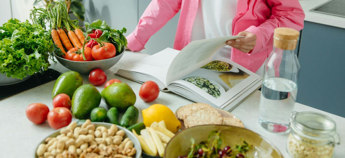Person browsing a cookbook beside fresh vegetables on the kitchen counter, suitable for an After Christmas Diet