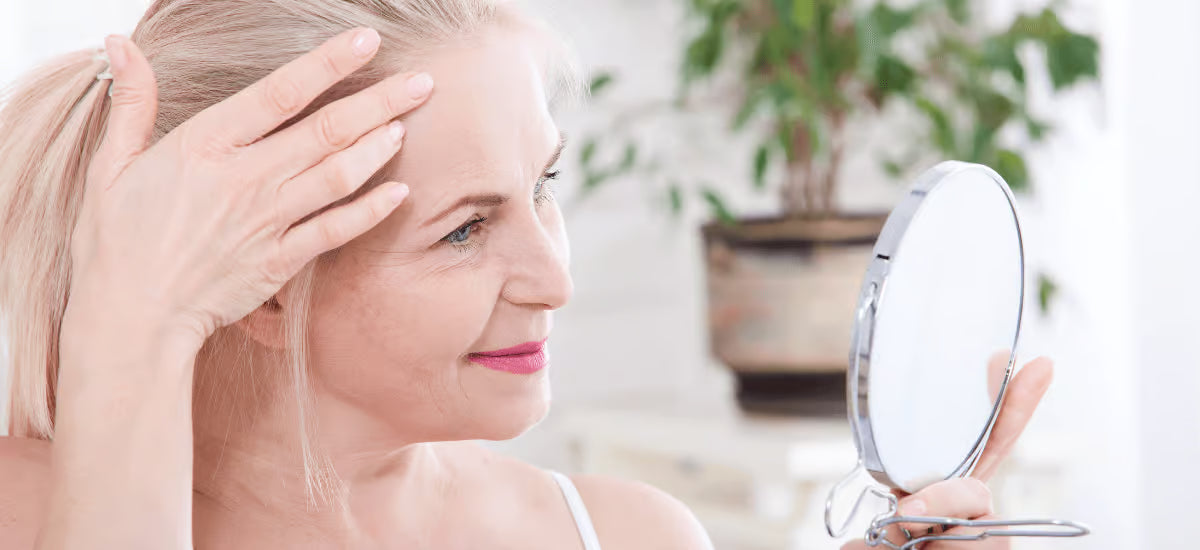 A smiling woman with healthy skin, nails and hair browsing in the mirror.