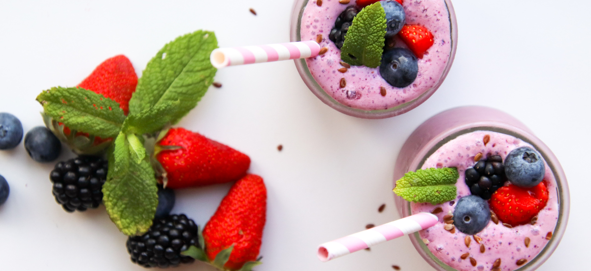 Healthy smoothies in glasses with straws, decorated with mint leaves, blueberries, strawberries and blackberries on a white background.