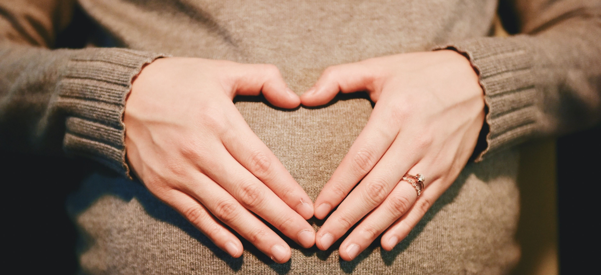 Pregnant woman forming a heart shape on her belly while using Primabiotic Collagen