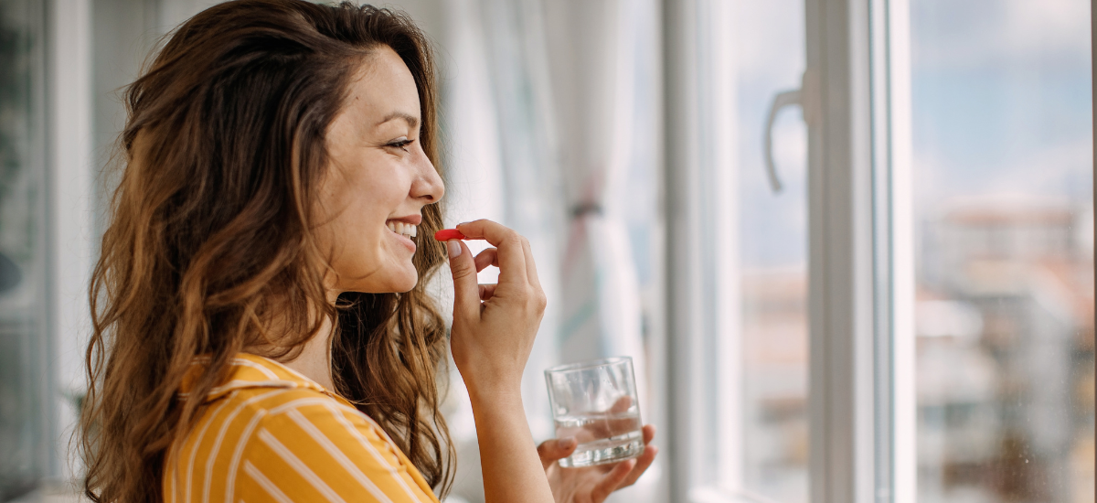 Smiling woman taking a dietary supplement with a glass of water in the morning