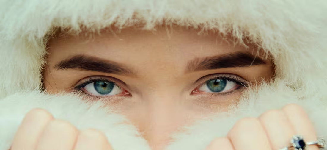 Close-up of blue-eyed woman wrapped in soft white fur, protecting her skin in winter