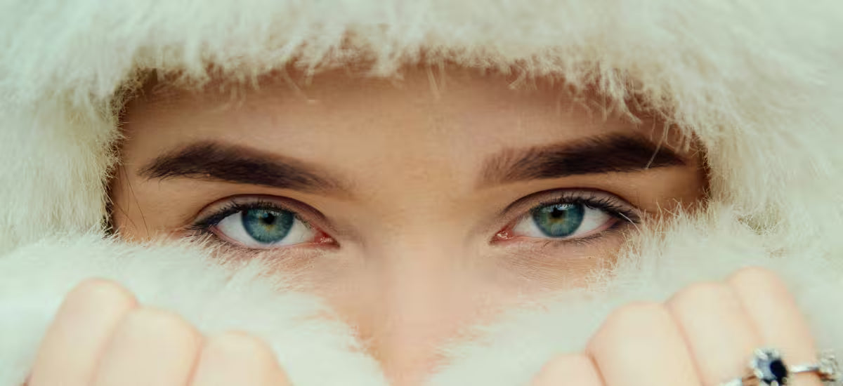Close-up of blue-eyed woman wrapped in soft white fur, protecting her skin in winter
