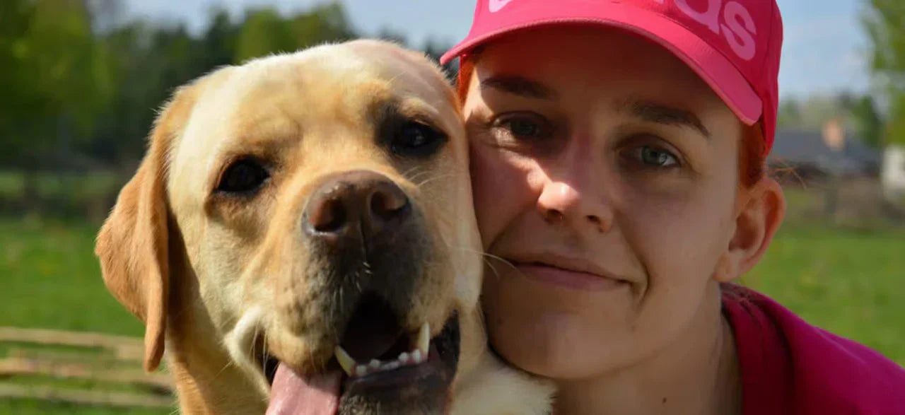 Woman in a pink cap smiling outdoors with a happy Labrador dog
