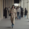 Stylish woman in a beige trench coat confidently walking through a city arcade, embodying natural beauty and elegance